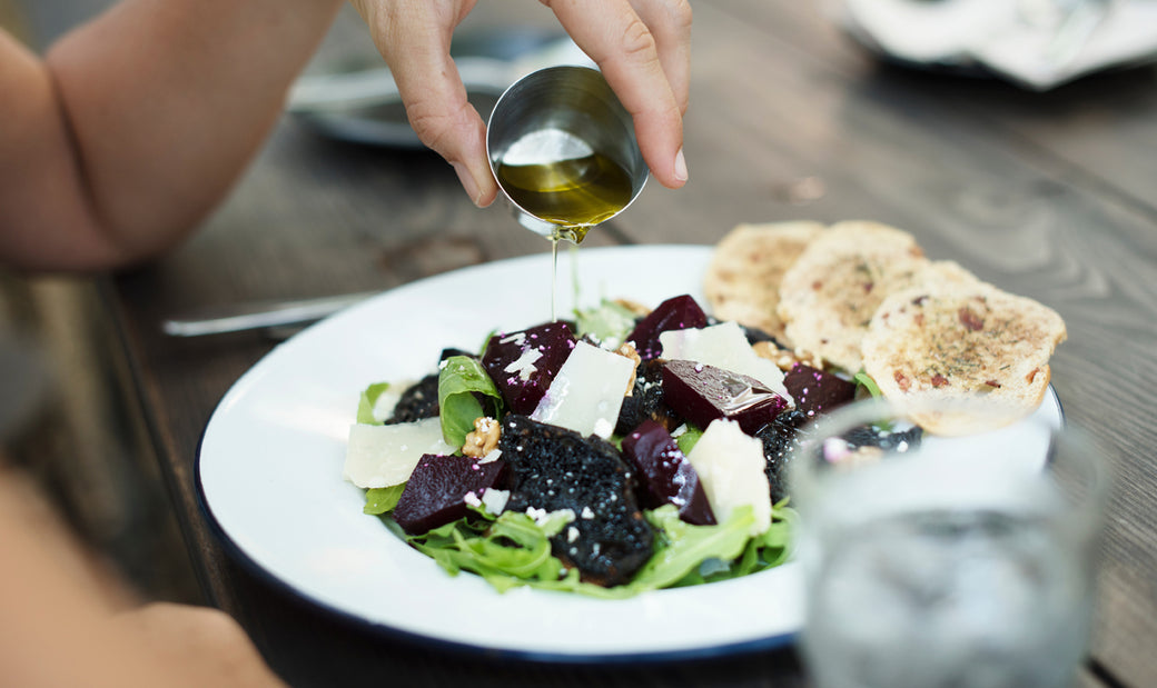 a woman drizzling dressing over a salad