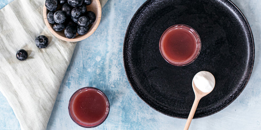 collagen powder on a spoon with blueberries and a smoothie