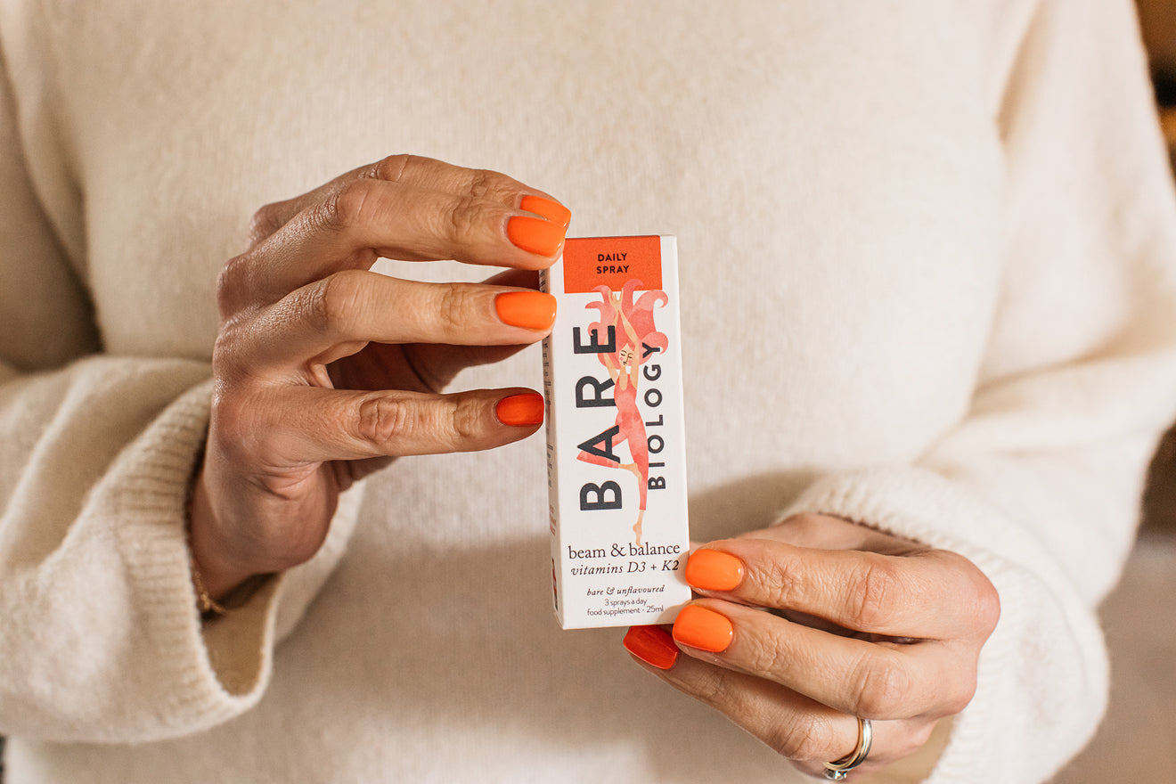 woman with orange nails holding bare biology's unflavoured vitamin d3 + k2 spray