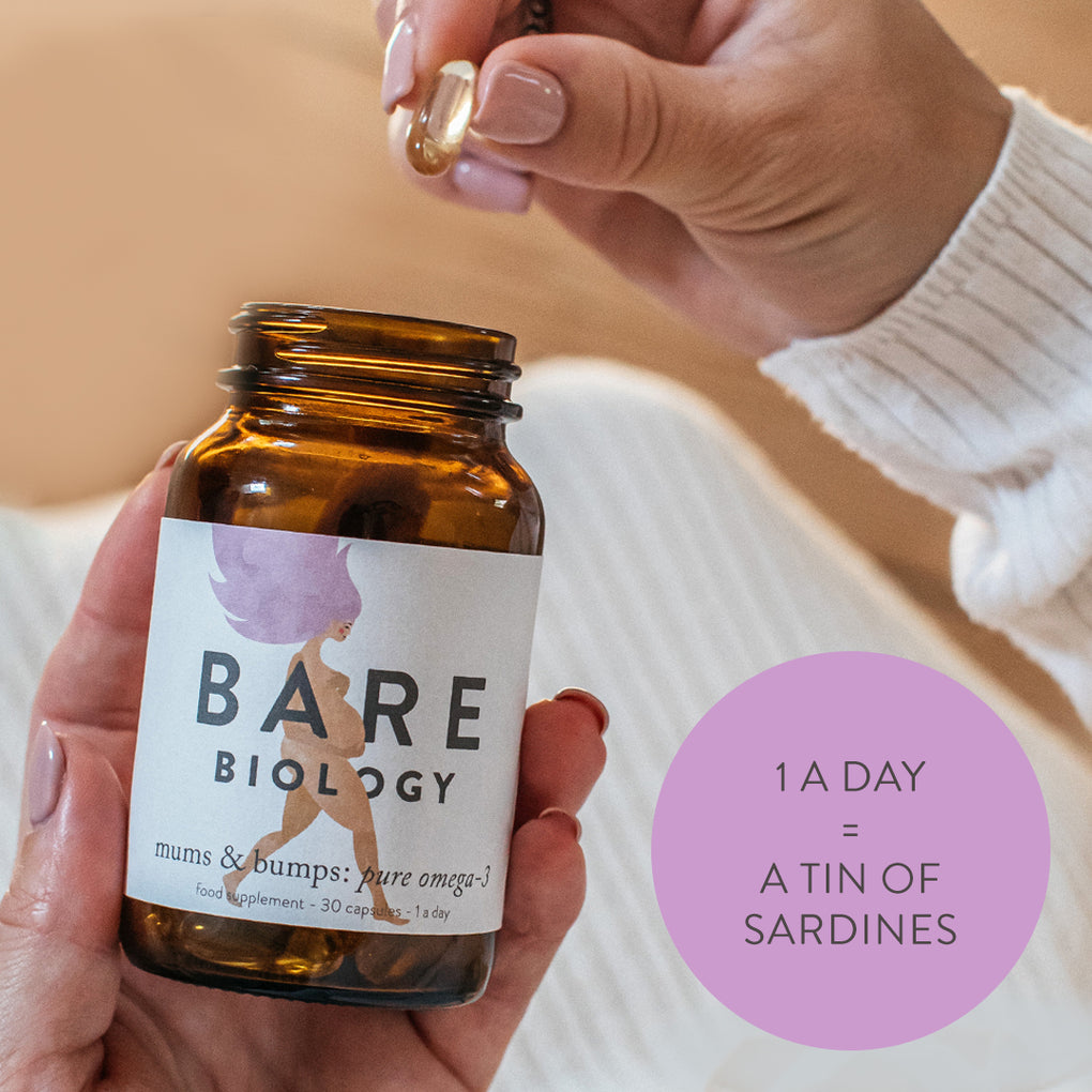 a woman holding jar of bare biology mums & bumps capsules in one hand and holding a capsule in the other. 1 a day = a tin of sardines is written in a purple circle in the bottom right corner. 