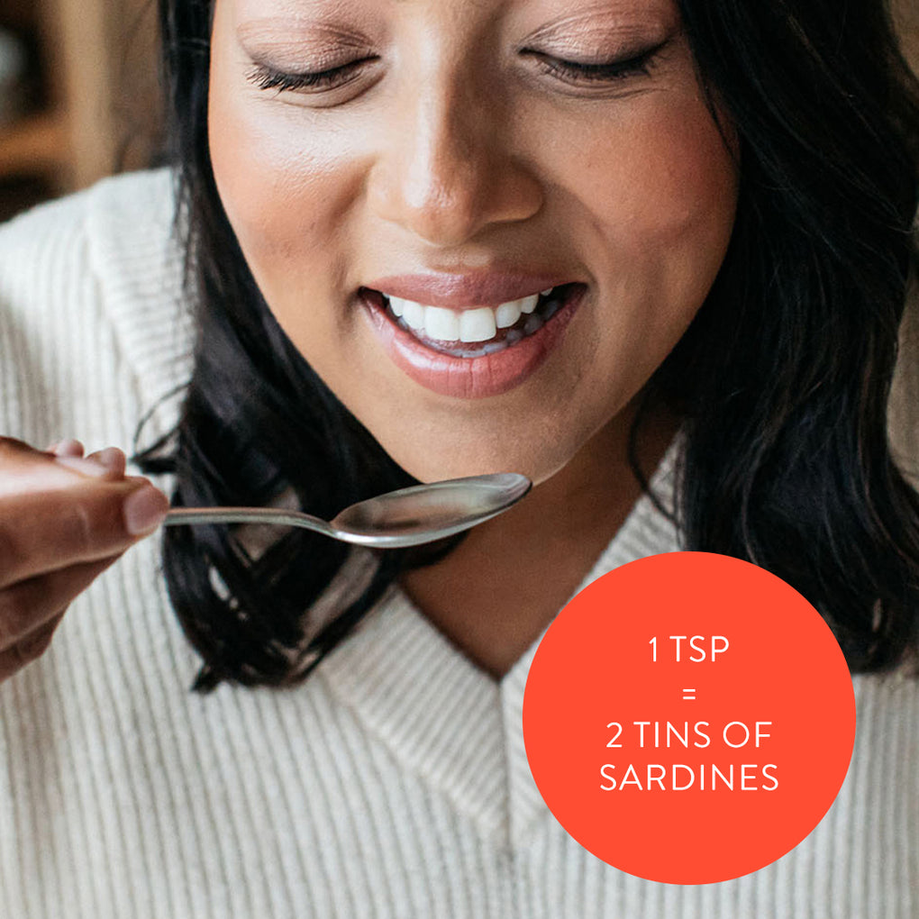 A lady taking Bare Biology's omega- fish oil liquid and an orange circle with dose advice: 1 tsp equals 2 tins of sardines.