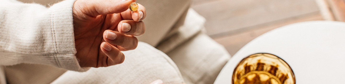 a woman holding a bare biology life & soul mini capsule with a glass of water in a yellow glass