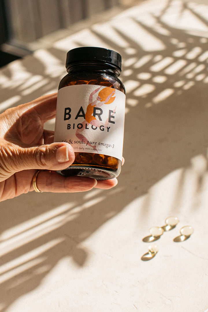 hand holding up a jar of bare biology omega 3 capsules with capsules and plant shadows in the background
