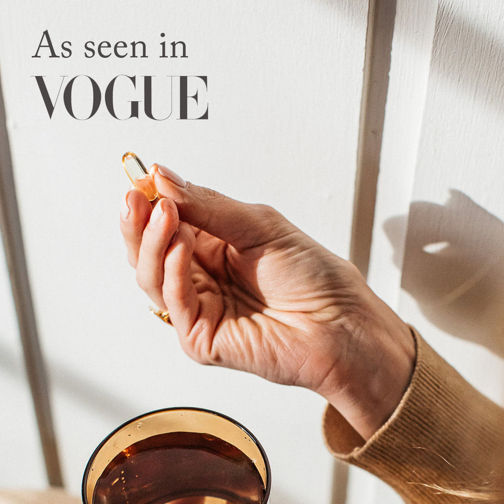 Womans hand holding a bare biology daily omega-3 capsule and a press feature: As seen in Vogue