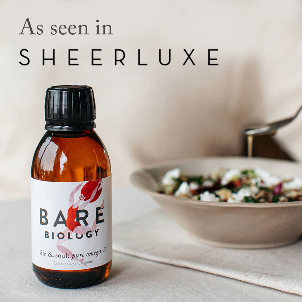 Bare Biology omega-3 fish oil liquid on a table with a blurred salad in the background and a press mention as seen in Sheerluxe above 