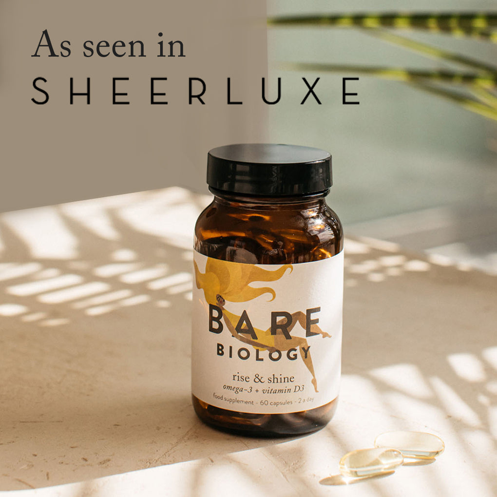 A jar of bare biology rise & shine on a marble table with sunny plant shadows, next to two capsules. Press feature: As seen in Sheerluxe.