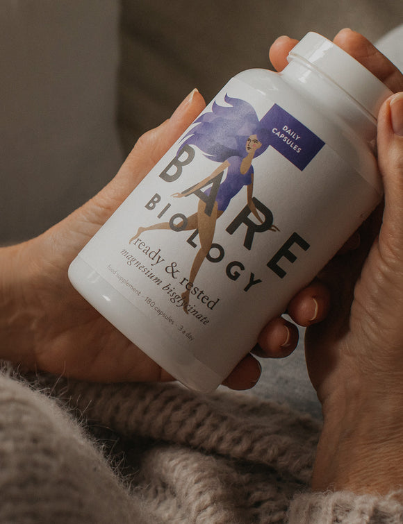 Close up of a woman's hands, wearing a brown knitted jumped and holding a jar of Bare Biology Ready & Rested magnesium capsules