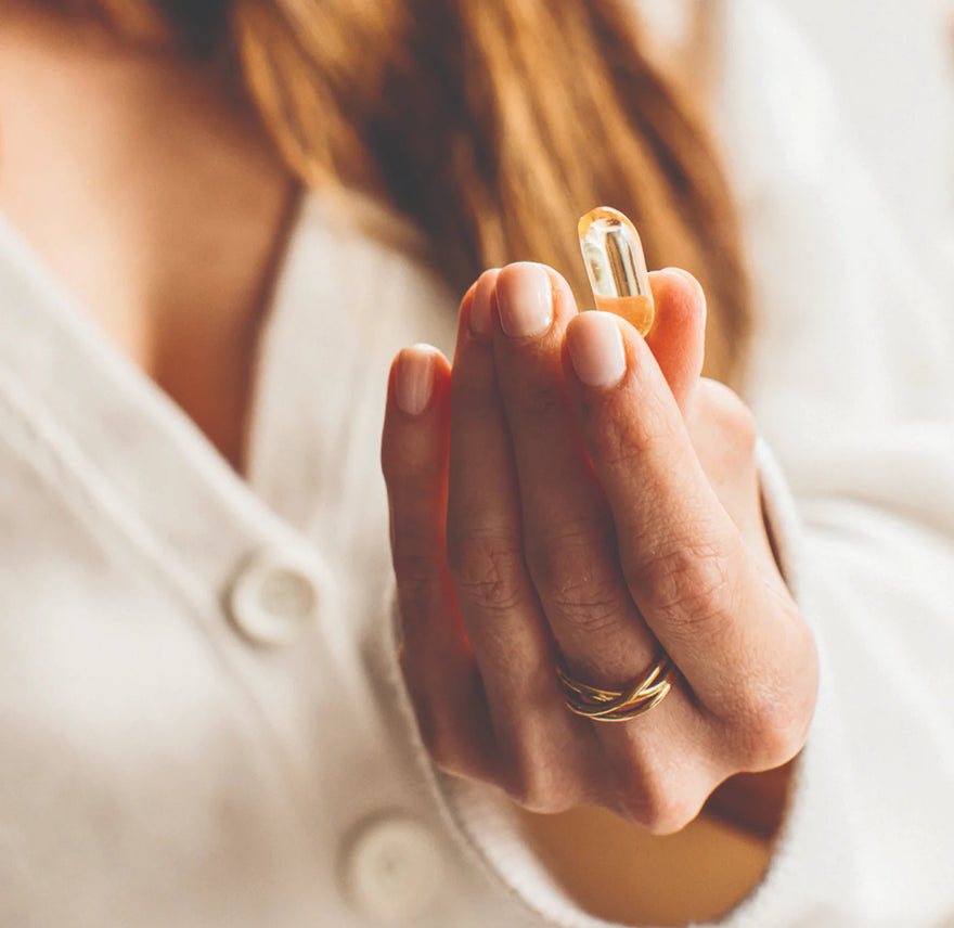 A woman in a cream jumper holding a bare biology life & soul omega 3 fish oil capsule