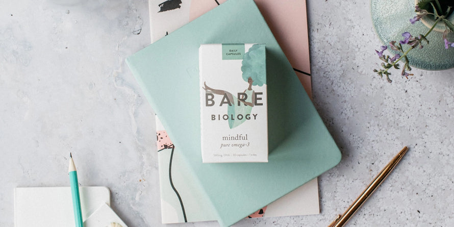 bare biology mindful omega 3 capsules box on notebooks with a gold pen and plant