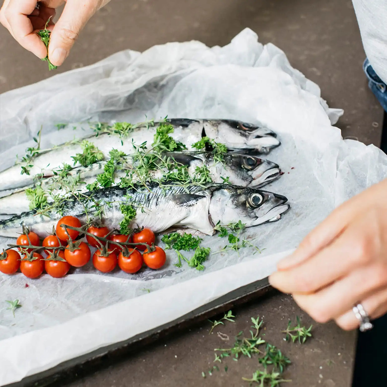 a row of fish with tomatoes and herbs on a baking tray